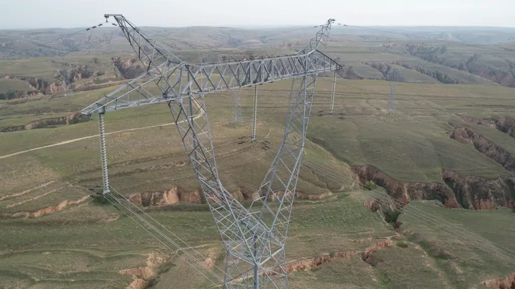 Aerial view of high voltage power transmission towers and lines spanning across green rolling hills and eroded valleys
