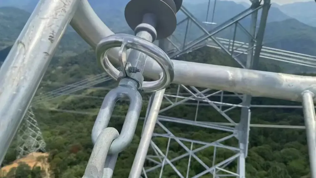 Close-up of high voltage transmission tower steel beams, insulators, and shackles against a mountain backdrop.