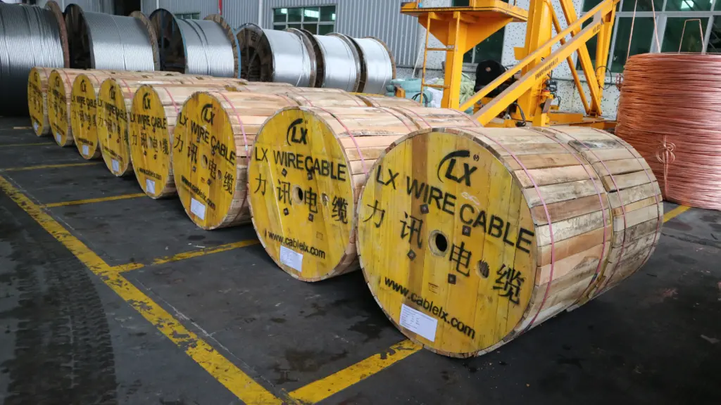 A row of large wooden cable spools labeled LX Wire Cable in a factory warehouse with copper and metal wire reels nearby.