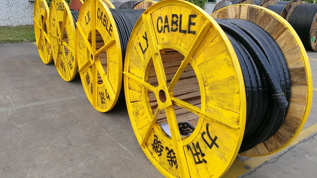 Large yellow cable reels labeled CABLE and LX wound with black cable, lined up outdoors on a concrete surface near a building